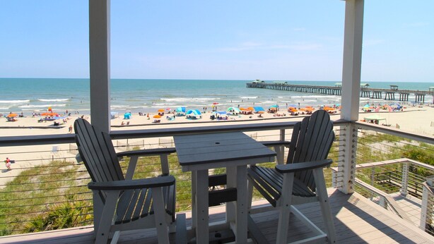 A beach view from a covered deck with two chairs and a table.
