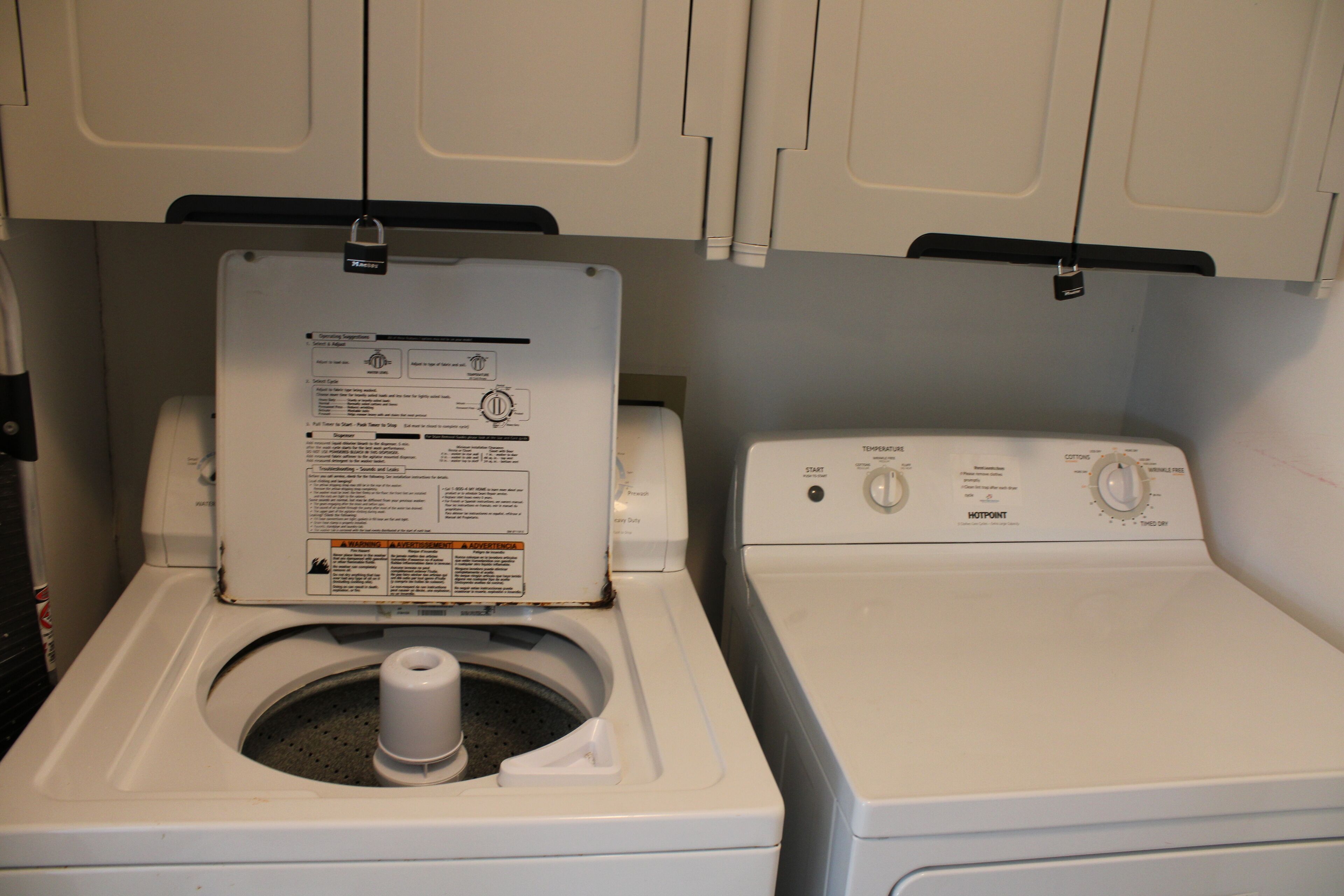 A front-loading washing machine and dryer in a laundry room with a cabinet above.