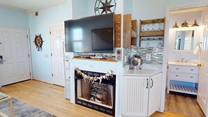 A living room with a fireplace, television, and a kitchen area with a sink and cabinets.