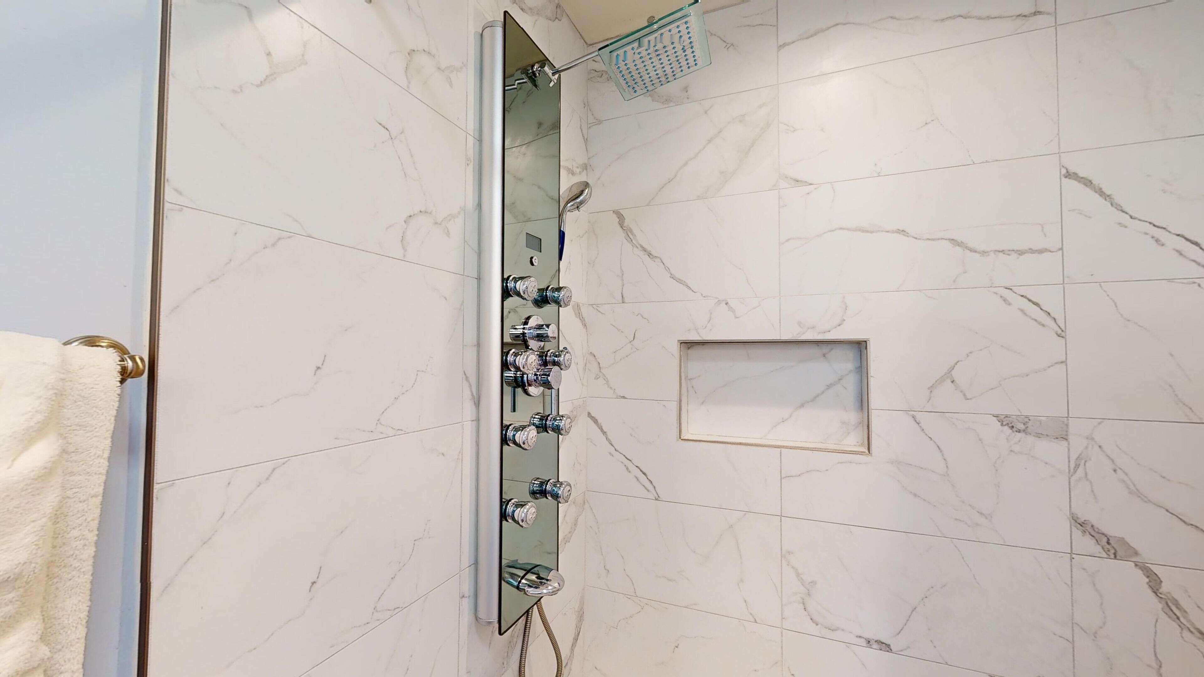 Un bagno moderno con cabina doccia in vetro, pareti in marmo e porta asciugamani.