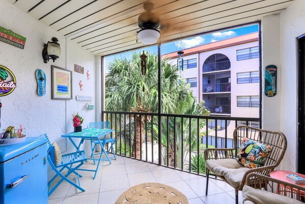 Un balcon avec des chaises bleues, un fauteuil en osier et une petite table.