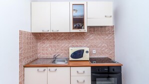 A compact kitchen with white cabinets, a microwave, a sink, and a stove. - Apartment Italia (Dubrovnik)