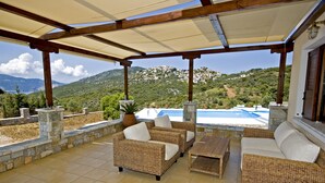 A covered outdoor seating area with wicker furniture and a view of a mountainous landscape. - Villa Manolia (Alonissos)