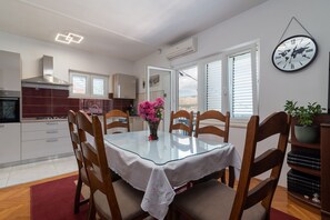 A modern kitchen with white cabinets, a stainless steel range hood, and a dining area with a glass table and wooden chairs.