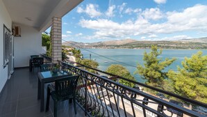 En balkon med et bord og stole med udsigt over en sø, med bygninger og bakker i baggrunden.