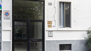 Een gebouwentree met een zwarte deur, een verbodsbord voor parkeren en een plaquette aan de muur.