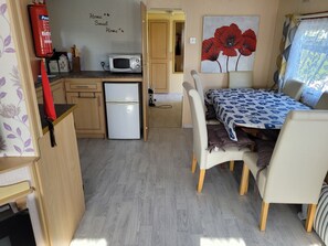 A compact kitchen with a microwave, refrigerator, and a small cabinet. There is a dining area with a table and chairs, and a painting of red flowers on the wall.