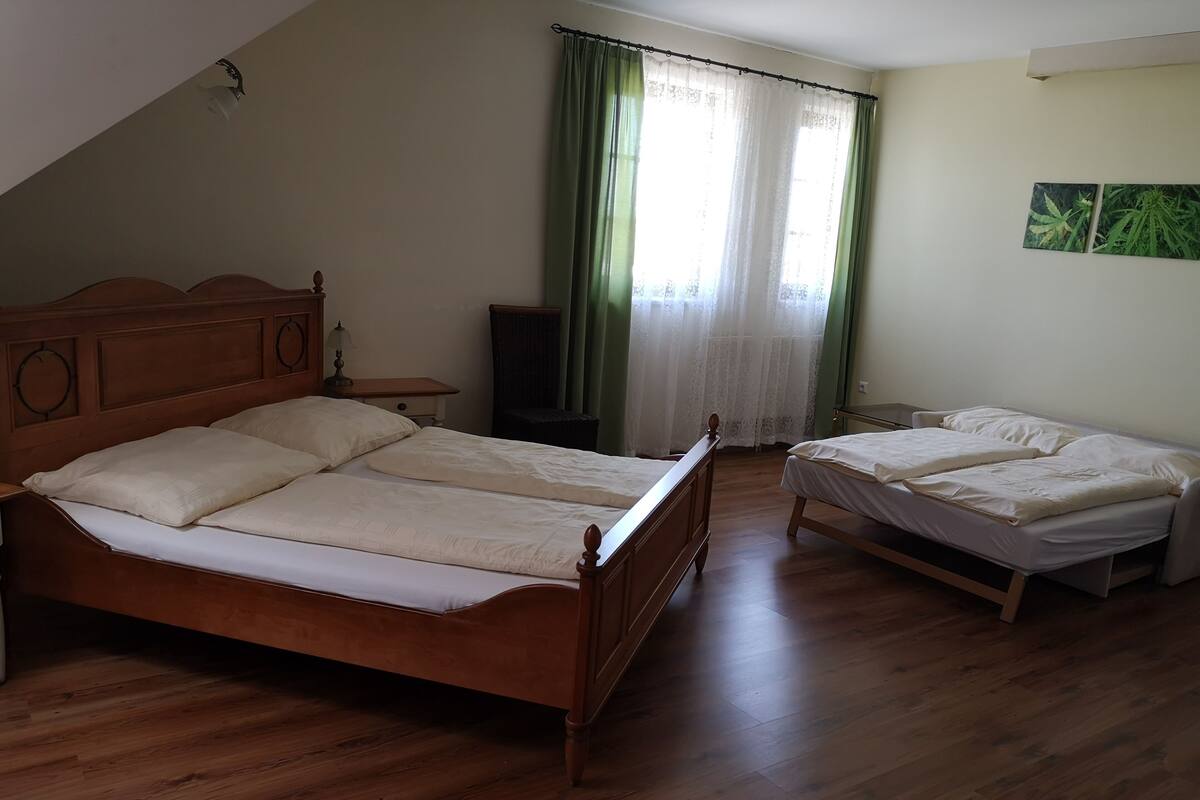 A bedroom with two wooden beds, a nightstand, a lamp, and a window with green curtains.