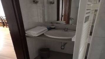 A small bathroom with a sink, mirror, and a trash bin.