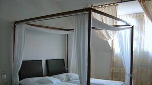 A four-poster canopy bed with white linens and sheer curtains, a bedside table with a lamp, and a window with sheer curtains. - Hanfthal-Hof (Laa an der Thaya)