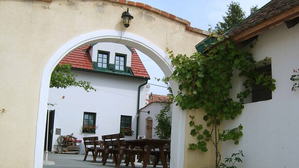 A courtyard with a white building, a red-tiled roof, and a wooden bench area. - Hanfthal-Hof (Laa an der Thaya)