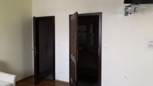 A room with two open doors leading to closets, a flat-screen TV mounted on the wall, and a white couch. - Hanfthal-Hof (Laa an der Thaya)