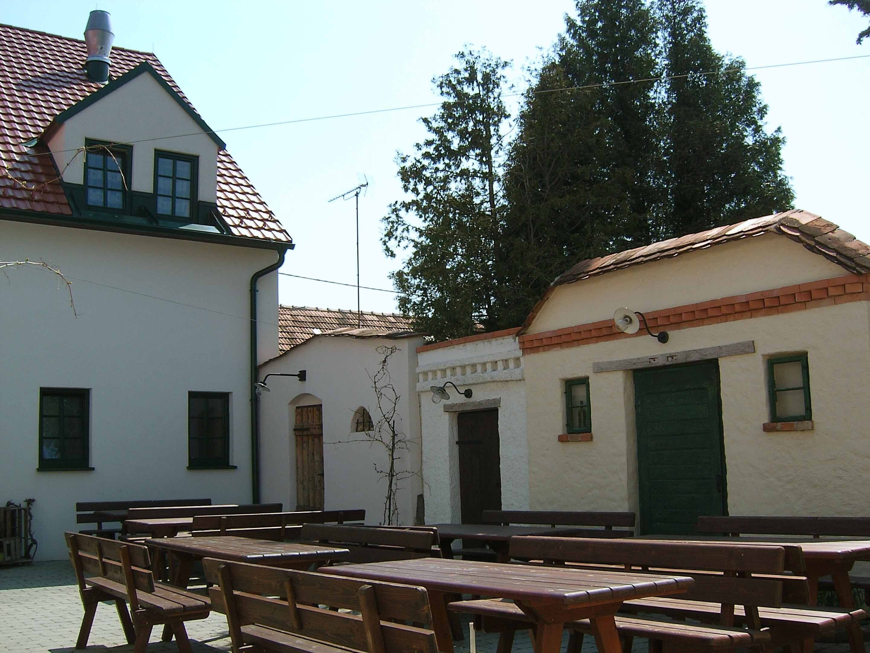 A building with a tiled roof, a green door, and a small window. There are wooden benches and tables outside.