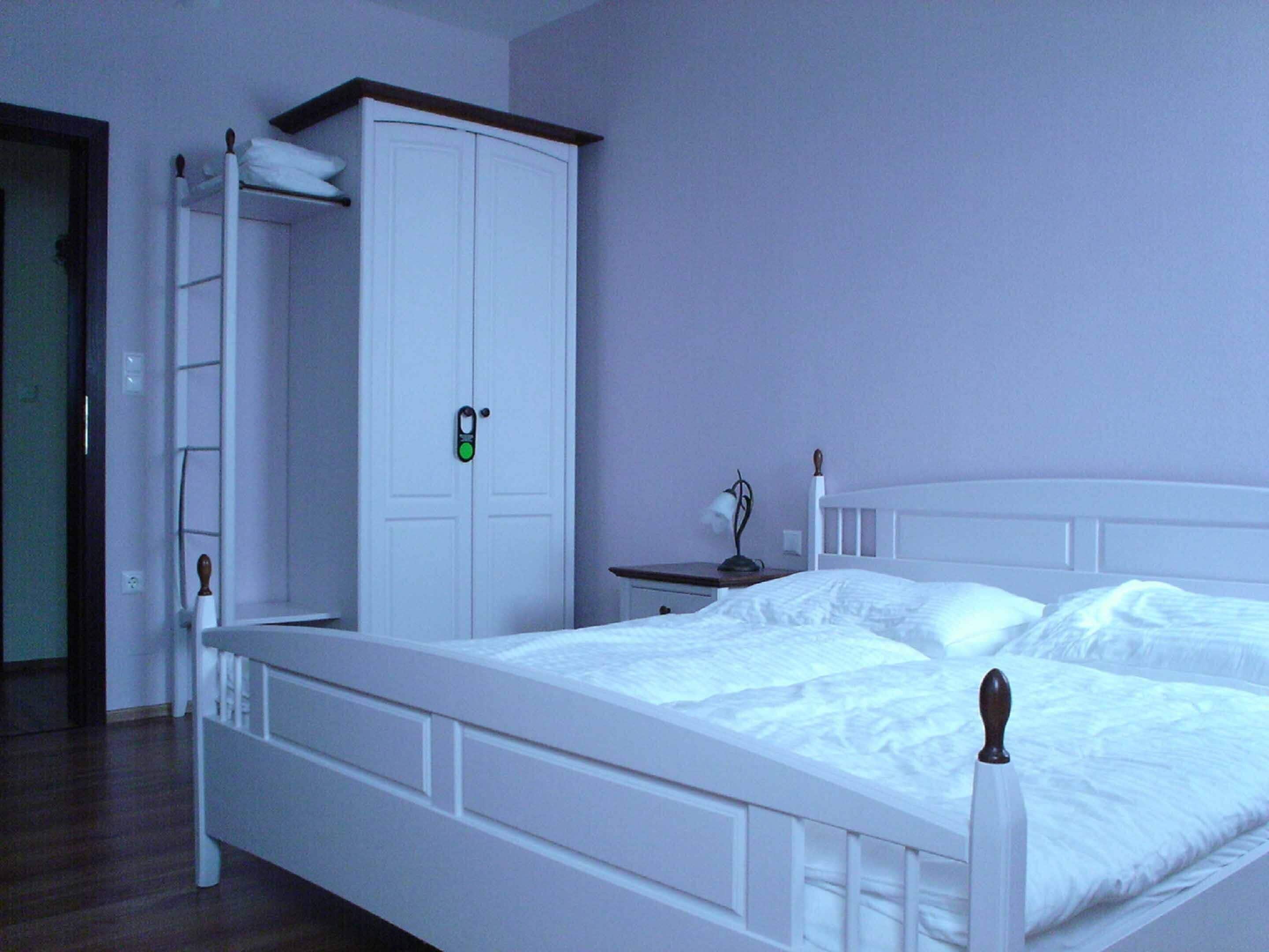 A bedroom with a white bed, a wardrobe, and a bedside table with a lamp.
