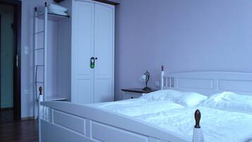 A bedroom with a white bed, a wardrobe, and a bedside table with a lamp.