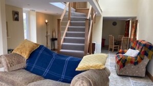 A living room with a sofa, a chair, a staircase, and a dining area. - Cosy 2-bed Cottage With Garden Near Carlisle (Carlisle)