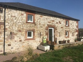 A stone building with a door, two windows, and a small garden area with potted plants.