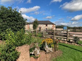 A rustic stone building with a wooden fence, surrounded by greenery and a clear sky.