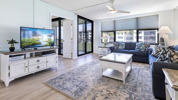 Un salon moderne avec un téléviseur à écran plat, un meuble de rangement blanc, un canapé bleu et une table basse en verre.