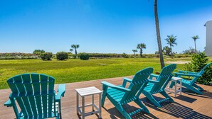 Une terrasse dotĂ©e de chaises Adirondack turquoise et dâune petite table, offrant une vue sur une pelouse bien entretenue et des palmiers.