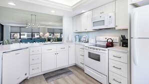 Une cuisine moderne avec des meubles blancs, un four à micro-ondes encastré, une bouilloire et un lave-vaisselle.