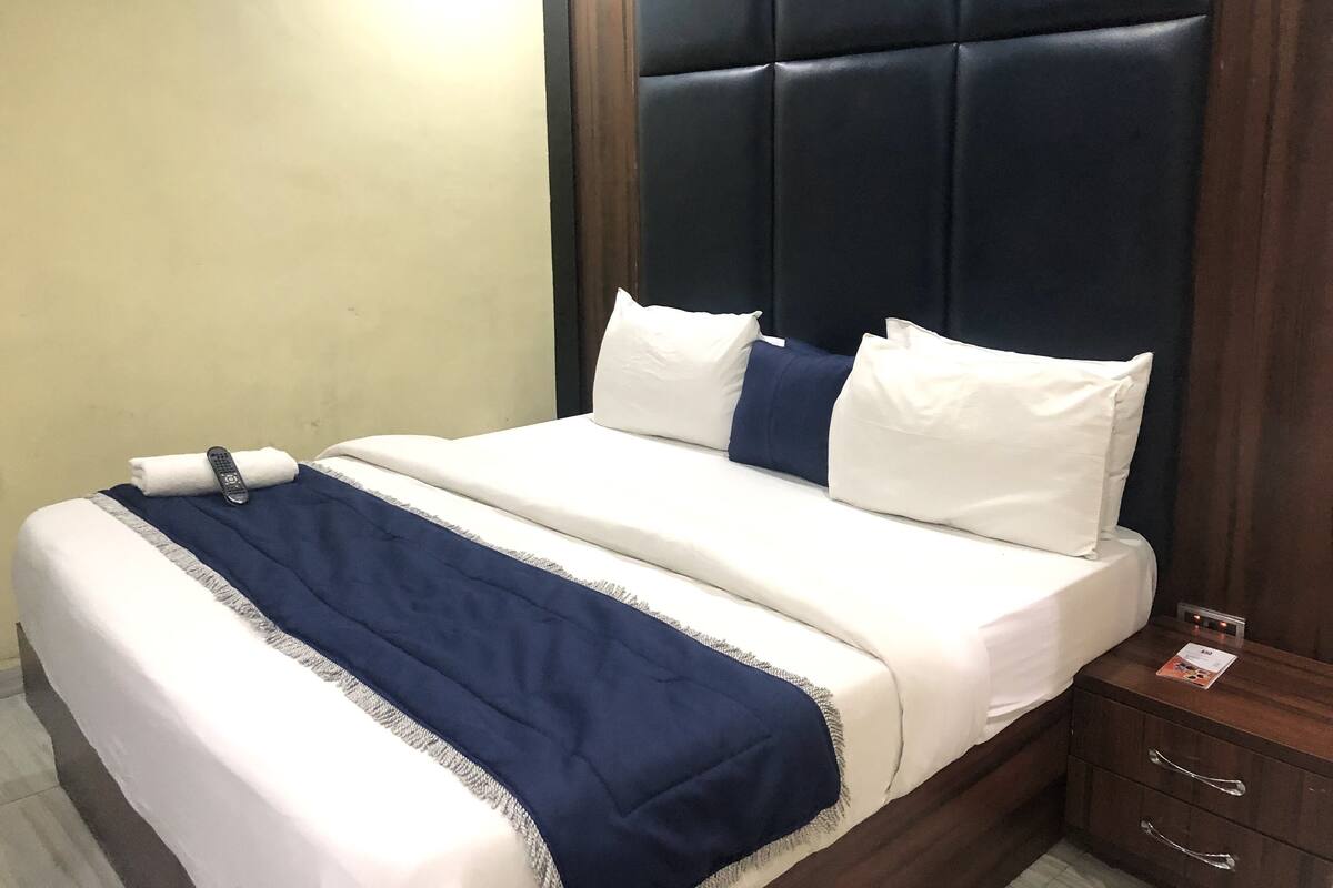 A hotel room with a bed, a nightstand, and a wall-mounted control panel.