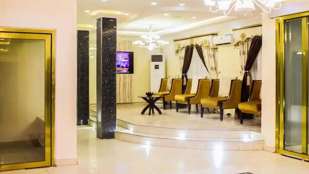 A lobby with a reception desk, a TV screen, and a seating area with chairs. - Six Diamond Hotel (Lagos)