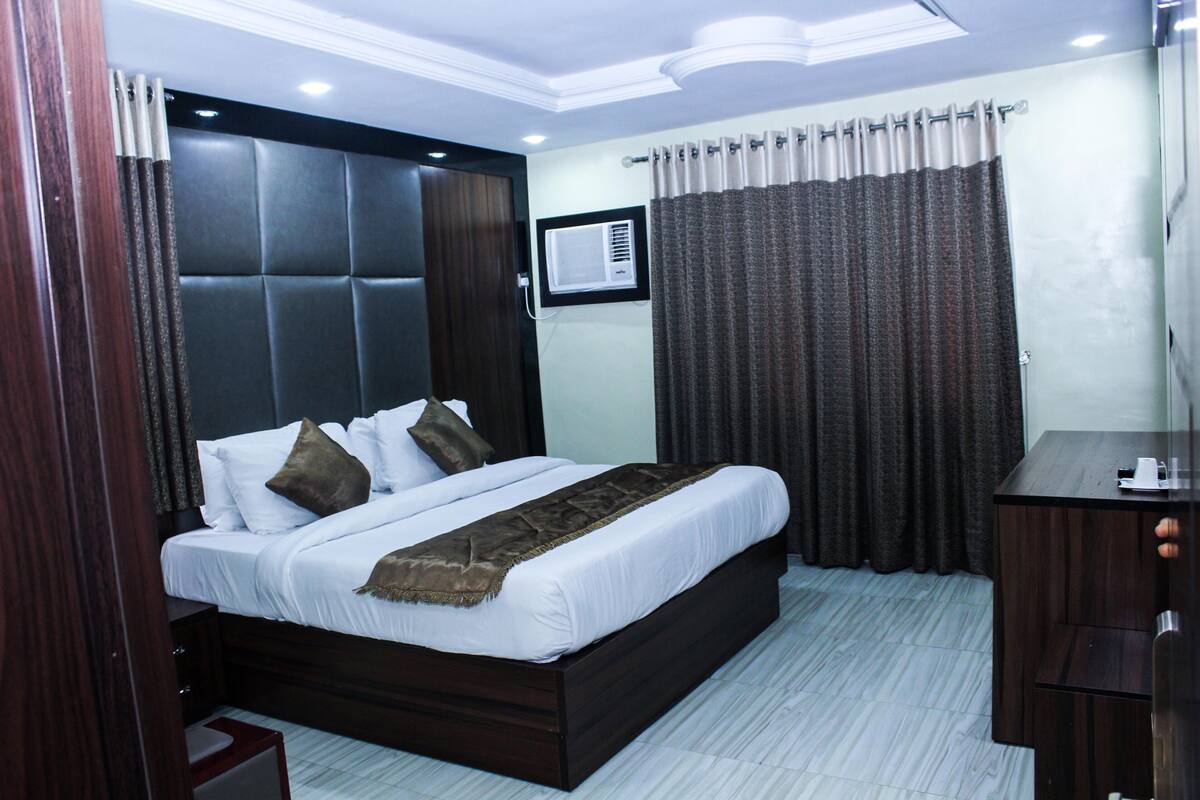 A hotel room with a bed, a desk, and a window with curtains.