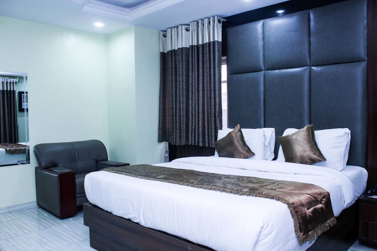 A hotel room with a bed, a chair, a nightstand, a mirror, and a window with curtains.