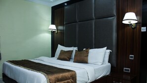 A neatly made bed with a brown throw blanket, a dark headboard, and two wall-mounted lamps. - Six Diamond Hotel (Lagos)