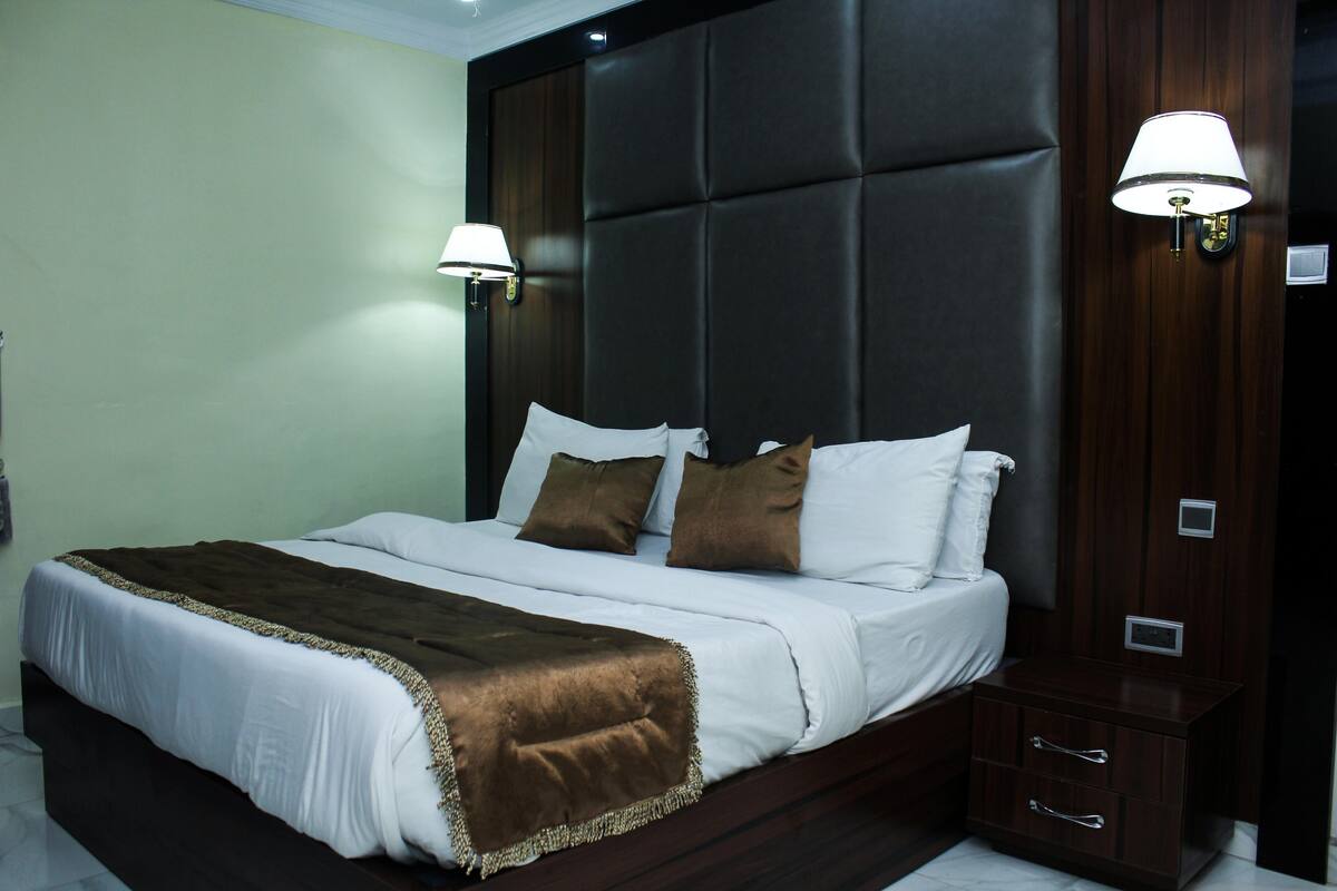 A neatly made bed with a brown throw blanket, a dark headboard, and two wall-mounted lamps.