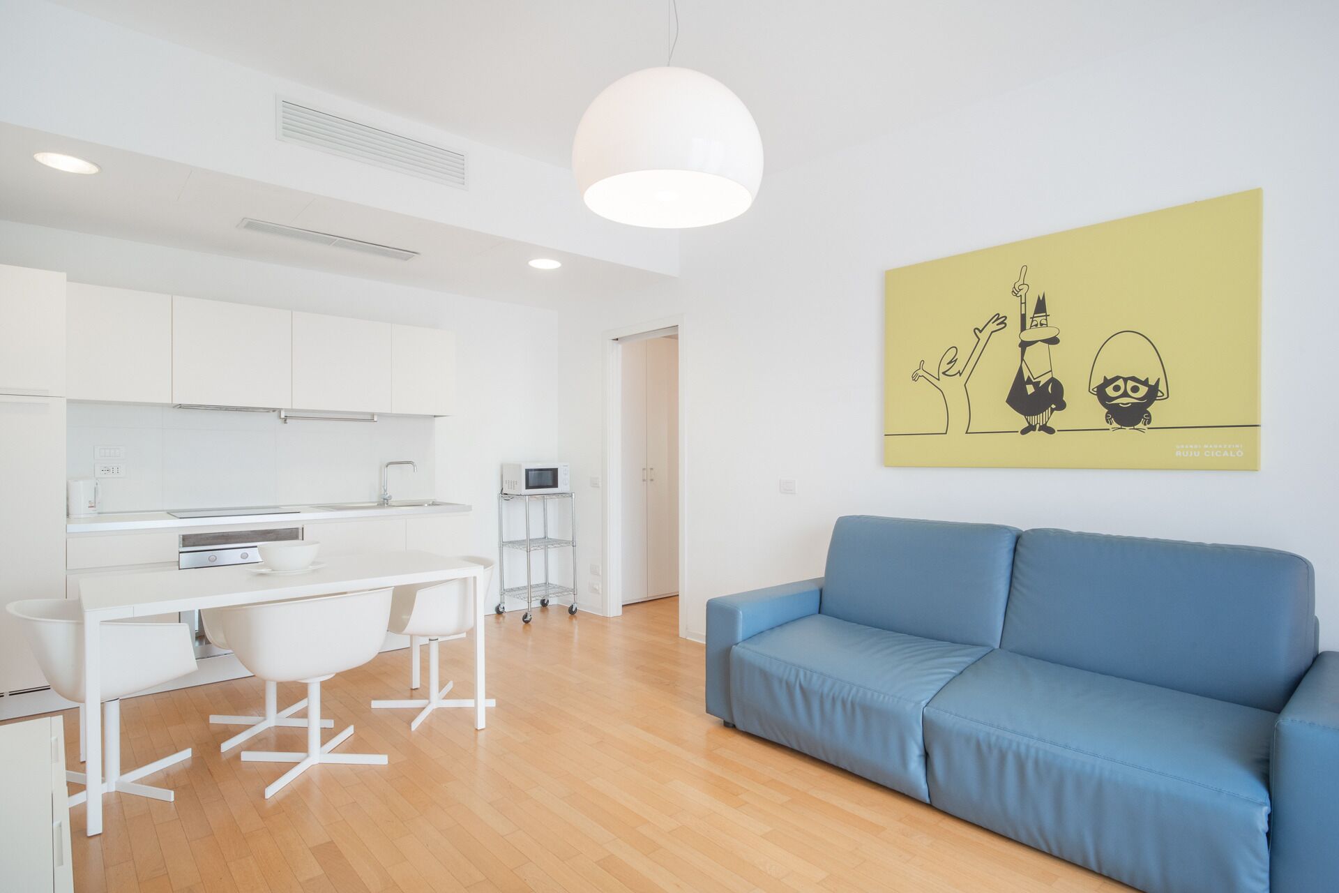 A modern, well-lit room with a blue sofa, a white desk with a computer, and a microwave on a cart.