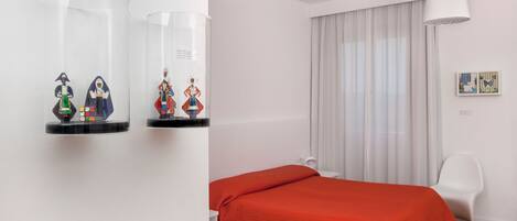 A modern bedroom with a bed, white walls, a window with curtains, and a white chair.