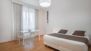 Een minimalistisch ingerichte slaapkamer met een bed, een bureau en een stoel.