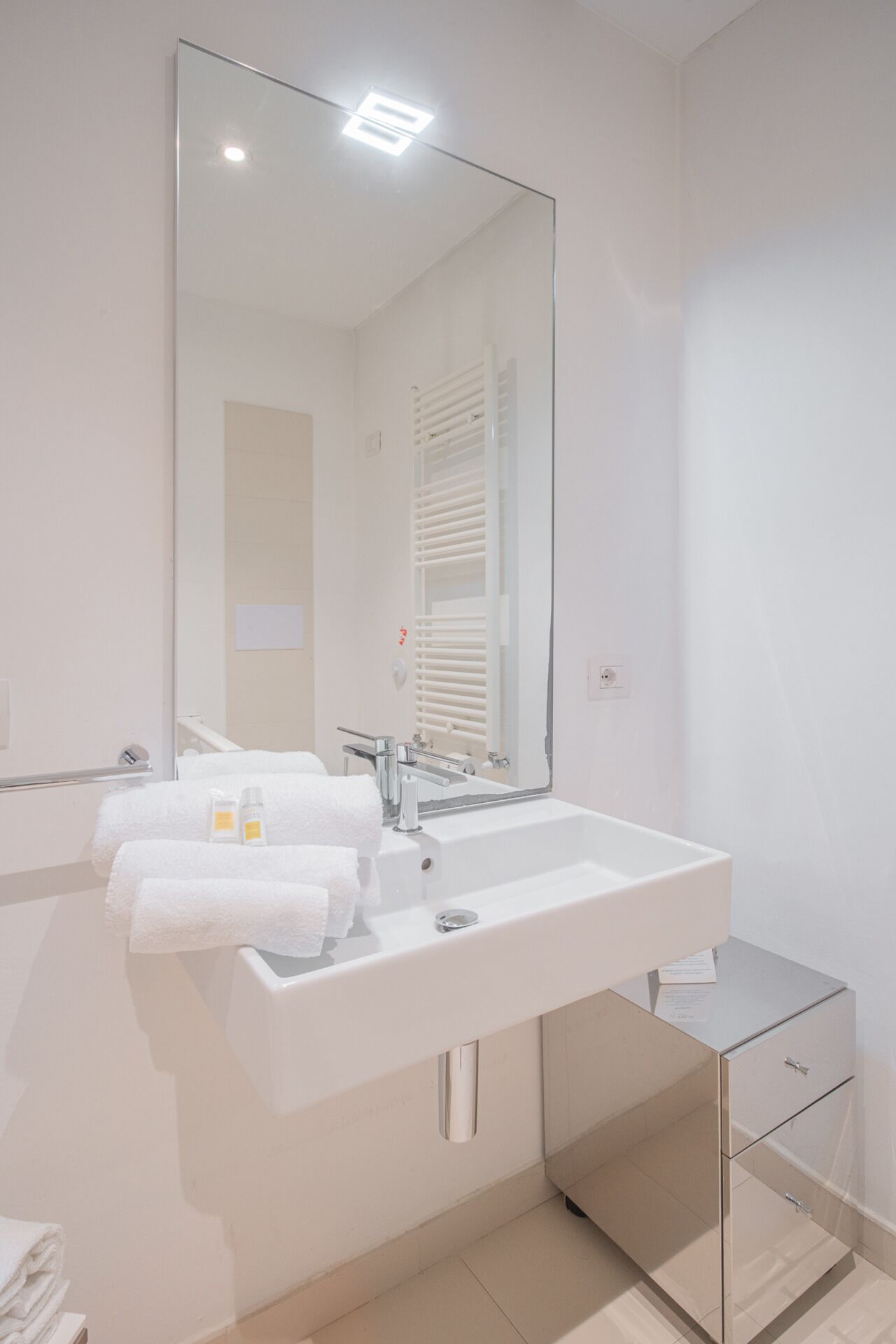Un baño moderno con un espejo grande, un lavamanos blanco y un armario de vidrio.