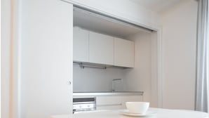 A modern kitchen with white cabinetry, a white dining table with two chairs, and a built-in oven. - Felix Hotels - Residence Grandi Magazzini (Nuoro)
