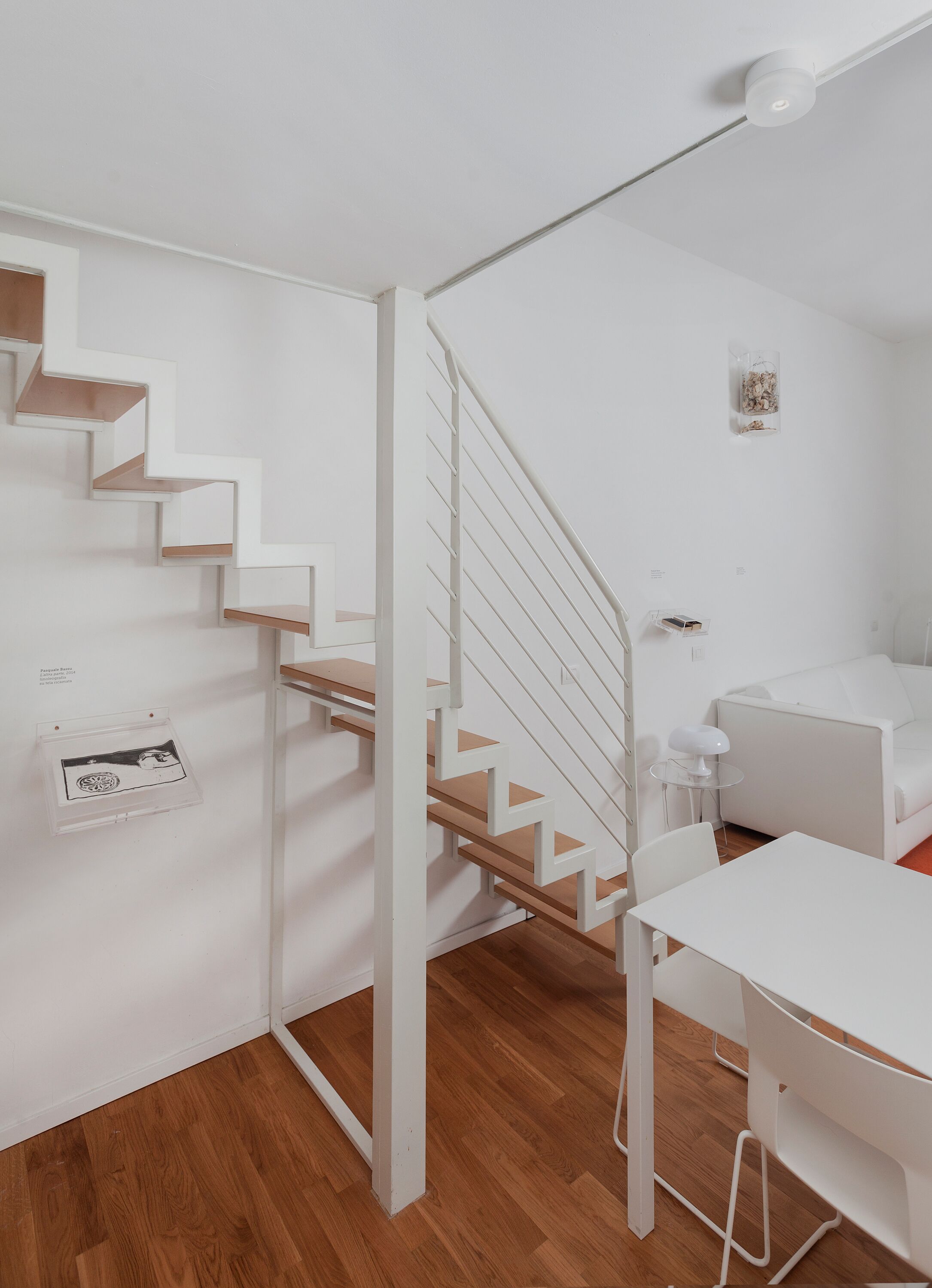 A modern, white interior with a wooden staircase, white walls, and a small table with a lamp.