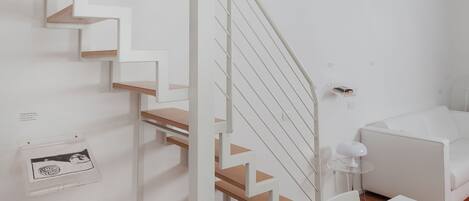 A modern, white interior with a wooden staircase, white walls, and a small table with a lamp.
