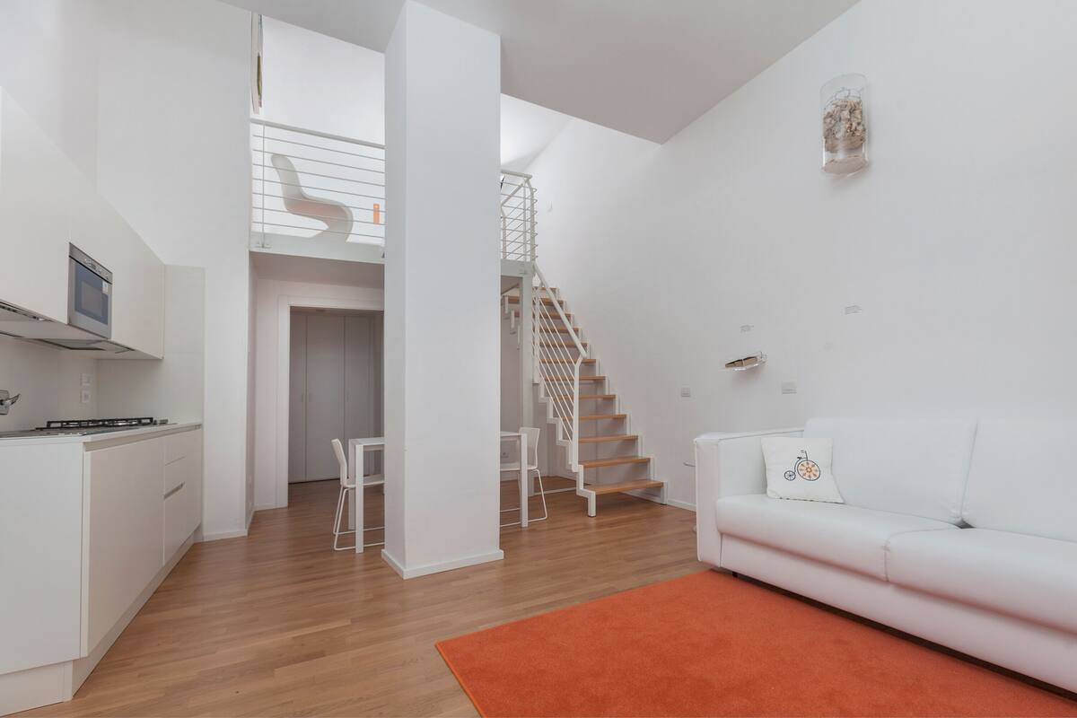 A modern, open-plan living space with a kitchen, dining area, and a staircase leading to an upper level.