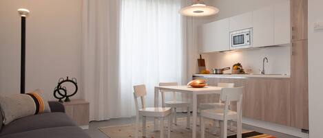 A modern, compact living space with a sofa, dining table, and chairs, a kitchen area with a microwave, and a pendant light.