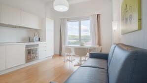 A modern kitchen with white cabinets, a microwave, and an oven. There is a dining area with a table and chairs, and a blue sofa. - Felix Hotels - Residence Grandi Magazzini (Nuoro)
