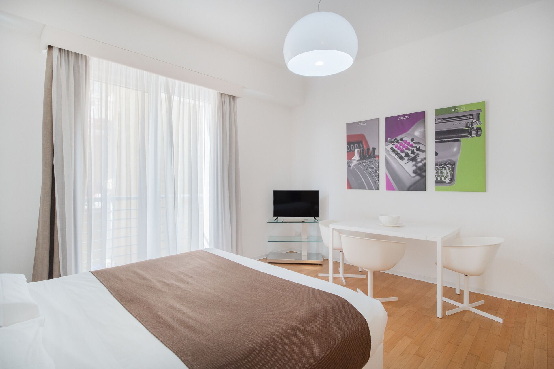 Una habitación de hotel moderna con cama, escritorio, dos sillas, televisor y obras de arte en la pared.