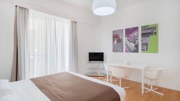 Una habitación de hotel moderna con cama, escritorio, dos sillas, televisor y obras de arte en la pared.