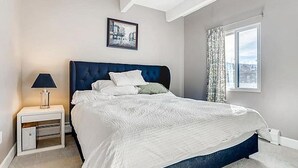 A bedroom with a large bed, a nightstand, a lamp, a framed picture on the wall, and a window with curtains. - Steps from Main St, quiet 2-bdrm condo w/views, fireplace, hot tub, steam shower (Frisco)