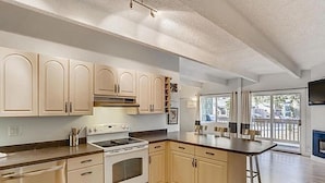 A modern kitchen with light-colored cabinets, a central island, and a large window providing natural light. - Steps from Main St, quiet 2-bdrm condo w/views, fireplace, hot tub, steam shower (Frisco)