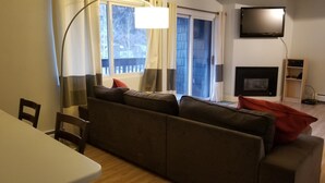 A living room with a sofa, a TV mounted on the wall, a fireplace, and a dining area with a table and chairs. - Steps from Main St, quiet 2-bdrm condo w/views, fireplace, hot tub, steam shower (Frisco)