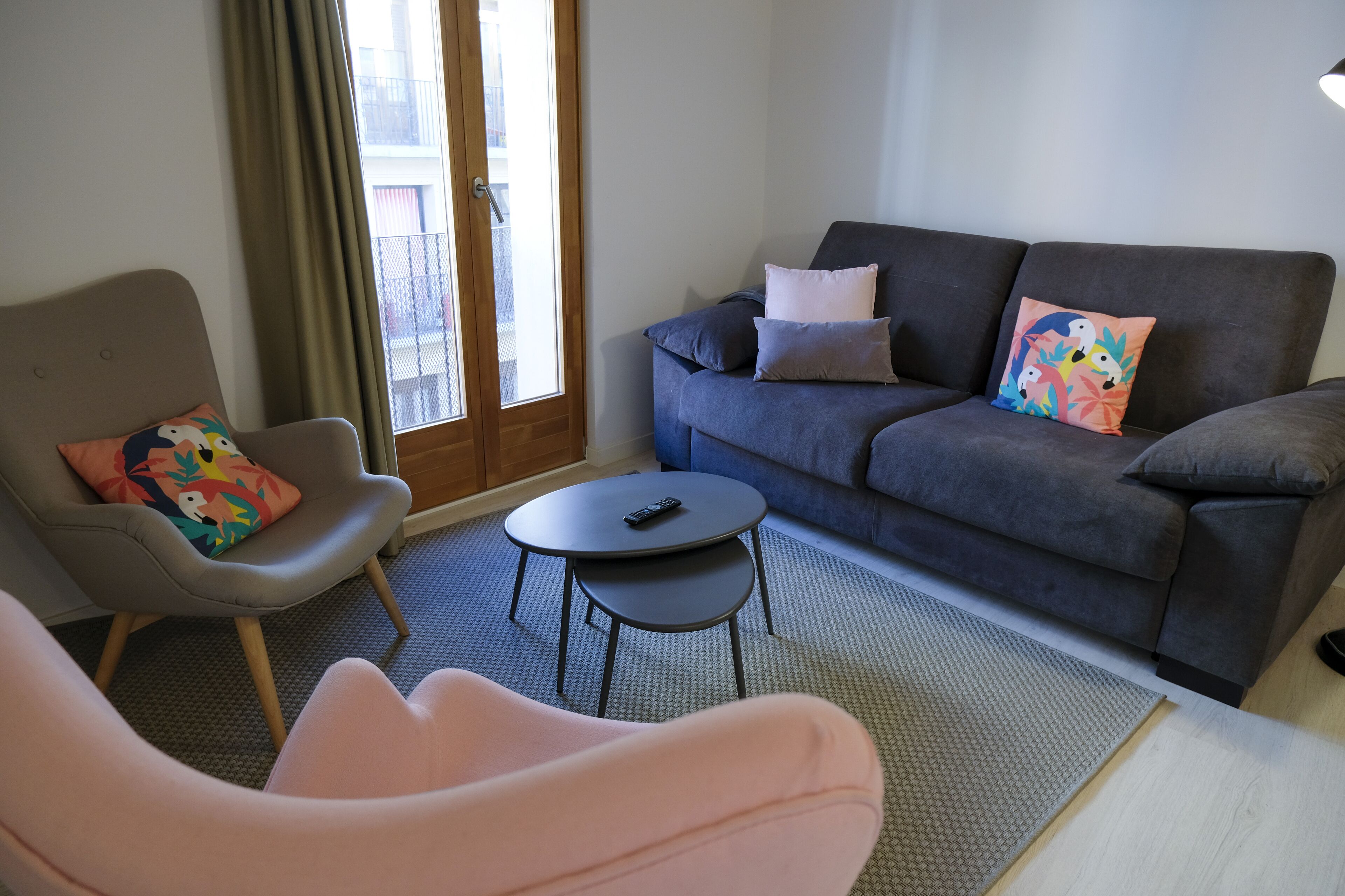 A living room with a grey sofa, a pink armchair, a small round table, and a colorful pillow.