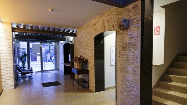 A hotel lobby with a brick wall, a wooden bench, a small table with a plant, and a staircase. - Silken Casa Platerias Siglo XV (Zaragoza)