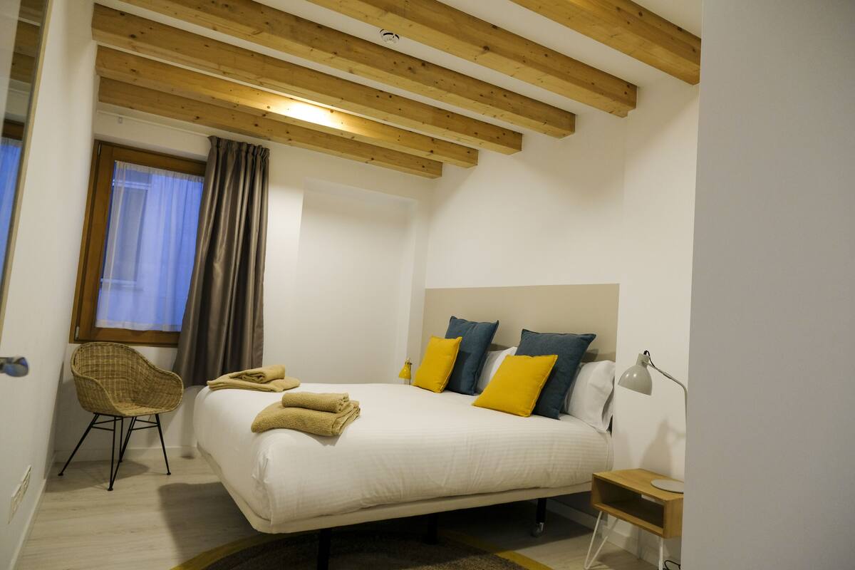 Un dormitorio con cama, una silla, mesita de noche y lámpara.