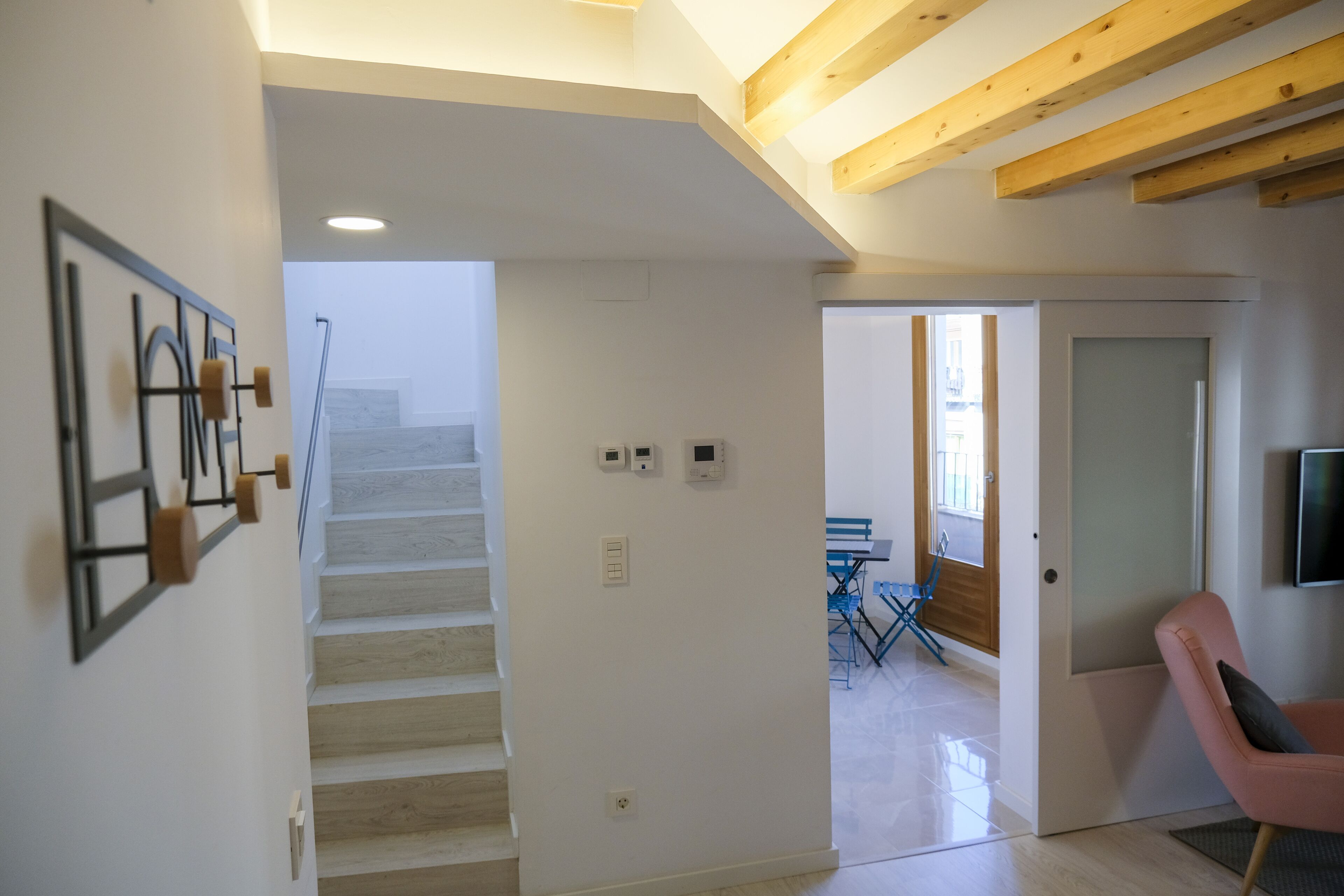 Una escalera conduce a un segundo piso con un interior moderno, que incluye una silla rosa y un comedor con sillas azules.